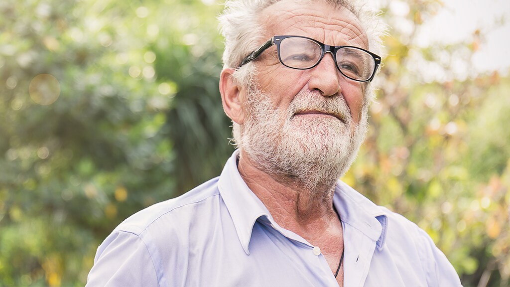 Ældre mand med hvidt skæg og briller. Han er iført lys blå skjorte og kigger op mod solen